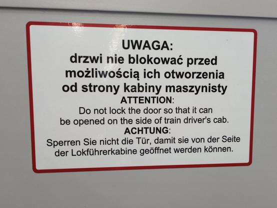 Komunikat w trzech językach. Po polsku:

"""
UWAGA: drzwi nie blokować przed możliwością ich otworzenia od strony kabiny maszynisty.
"""

Po angielsku:

"""
ATTENTION: Do not lock the door so that it can be opened on the aide of train driver's cab.
"""

Po niemiecku:

"""
ACHTUNG: Sperren Sie nicht die Tür, damit sie von der Seite der Lokführerkabine geöffnet werden können.
"""