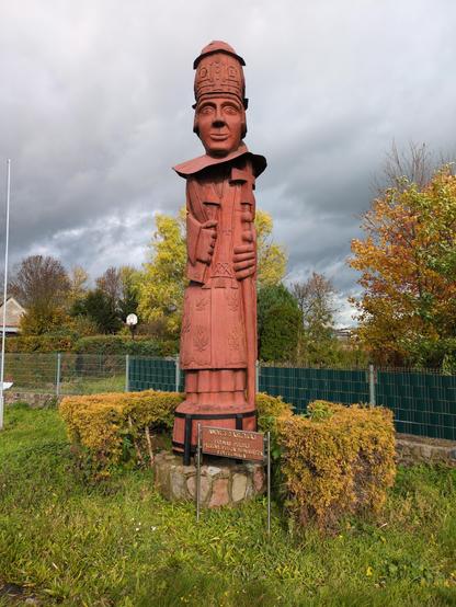 Totemiczna rzeźba, podpisana "Andrzej Krzycki. 1482–1537. Prymas Polski. Wybitny poeta, humanista i dyplomata."

Rzeźba wykonana jest z jasnobrązowego drewna na kamiennym cokole. Przedstawia mężczyznę w ozdobnej sutannie, z wielkimi dłońmi, płasko przylegającymi do figury. W jednej jest książka oraz pióro, w drugiej laska zakończona krzyżem. Na twarzy uśmiech, oczy szeroko otwarte, Na głowie mitra, a na jej wierzchu lekki kapelusz.

Rzeźbę otacza po bokach niski żywopłot, a dalej trawa. W tle o…