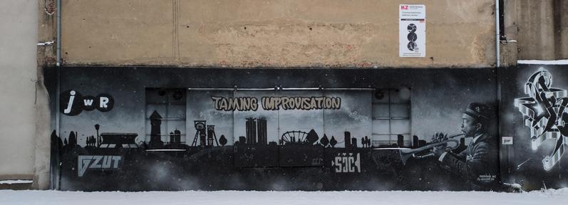 Mural na ścianie budynku. Przedstawia panoramę miasta w postaci czarnych konturów na tle srebrzystego nieba z padającym śniegiem. Widać na nim kontury drzew, stojących ludzi, budynków — wieży ciśnień, zabudowy kopalni, silosów. Po prawej w stronie widać stojącego znacznie bliżej mężczyzny w garniturze i kapeluszu, grającego na trąbce, również przedstawionego w kolorach szarości. Z czary wiją się nuty na pięciolinii.

Mural umieszczono na ścianie budynku z kremowym tynkiem, pokrywa również rynnę…