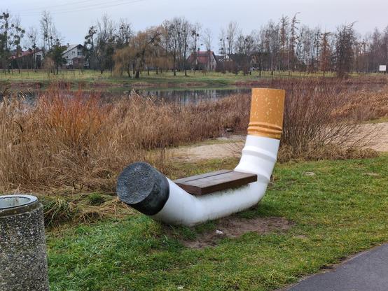 Ławka w kształt zduszonego niedopałka papierosa, nad jeziorem. Rama jest w centralnej części biała, przylega do ziemi. Po bokach unosi się do góry — z jednej strony końcówka pomalowana jest na pomarańczowo, z drugiej na czarno. Pośrodku umieszczono drewniane siedzenie.