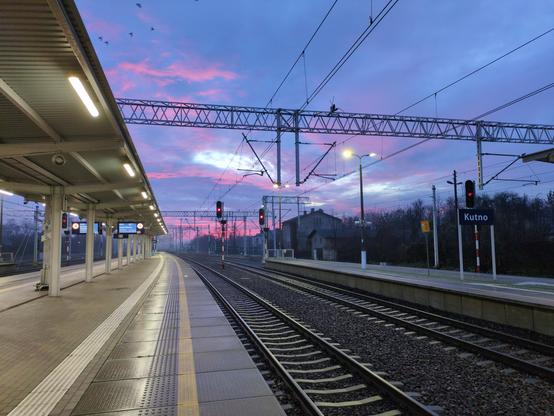 Rzut wzdłuż peronu wczesnym rankiem. W centralnej części dwa tory kolejowe, skręcające lekko w lewo, z semaforami sygnalizującymi na czerwono. Po lewej mokry peron z zadaszeniem, na powierzchni którego równolegle zawieszone oświetlenie tworzy linię odbitego światła przy krawędzi peronu. Po prawej niebieska, wąska tabliczka "Kutno". U góry sieć trakcyjna na tle kolorowego nieba. Nad horyzontem i na krawędziach ciemnoniebieskich chmur niebo jest czerwone, w bezchmurnych miejscach jasnoniebieskie.
