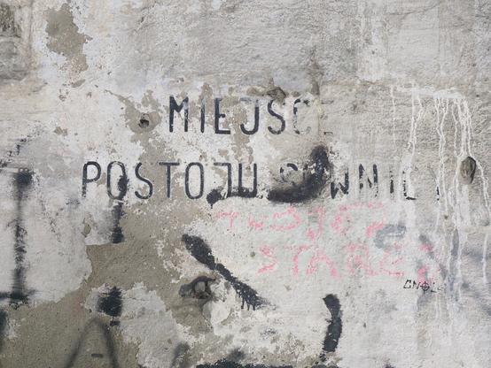 Mocno starty napis na ścianie "miejsce postoju suwnicy". Pod spodem ktoś dopisał "twojej starej".